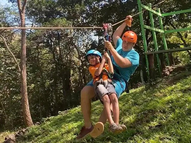 A helmeted guest rides a zipline through the forest canopy.