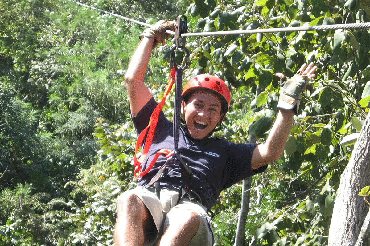 A helmeted guest rides a zipline through the forest at Canopy Monkey Jungle.