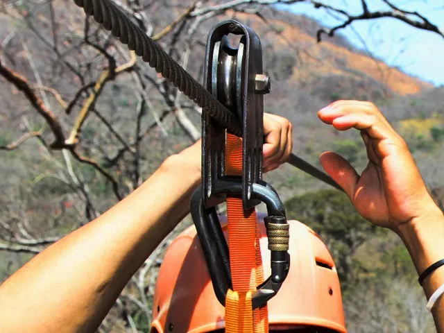 A gloved hand steadies the zipline trolley and cable.